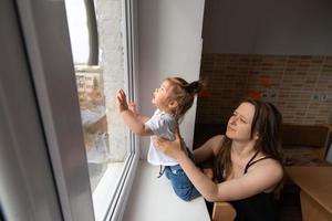 la niña mira por la ventana y pregunta afuera durante la cuarentena causada por el coronavirus.