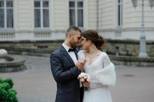 feliz pareja de bodas de lujo besándose y abrazándose cerca de retro con coche de ramo en otoño foto