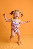A little girl dressed in a swimsuit at the age of one and a half years is jumping or dancing. The girl is very happy. Picture taken in the studio on a yellow background. photo