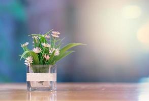 Plastic flowers in clear vase on table on bokeh background photo