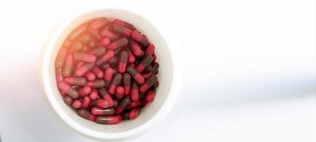 Cápsulas marrones rojas en frasco blanco en el concepto de farmacia de atención médica, cerrado foto