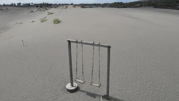 vista aérea del viejo columpio de madera de cuerda en el desierto o en la playa de arena con fondo de montaña video