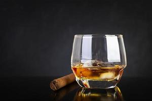 Glass of whiskey and cigar on dark background. photo