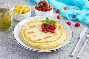 Pancakes with caramelized apples, raspberries, strawberries and red currants. Brunch with green tea and crepes. photo