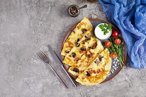 Delicious pancakes with mushrooms, ham and cheese, arugula, tomatoes and sour cream on a wooden background photo