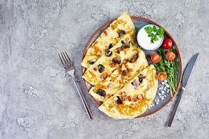 Delicious pancakes with mushrooms, ham and cheese, arugula, tomatoes and sour cream on a wooden background photo