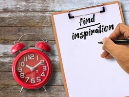Find inspiration handwritten on clipboard and red alarm clock on wood table