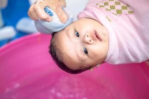 mamá asiática ducha al bebé para limpiar la suciedad dar al niño en un recipiente de baño para la limpieza estilo de vida familiar entre la madre y el niño utilizado para la ducha del bebé productos de crema champús lociones y productos para el cuidado del bebé foto