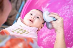 mamá asiática ducha al bebé para limpiar la suciedad dar al niño en un recipiente de baño para la limpieza estilo de vida familiar entre la madre y el niño utilizado para la ducha del bebé productos de crema champús lociones y productos para el cuidado del bebé foto