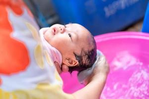 mamá asiática ducha al bebé para limpiar la suciedad dar al niño en un recipiente de baño para la limpieza estilo de vida familiar entre la madre y el niño utilizado para la ducha del bebé productos de crema champús lociones y productos para el cuidado del bebé foto