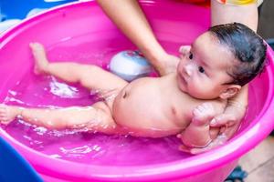 mamá asiática ducha al bebé para limpiar la suciedad dar al niño en un recipiente de baño para la limpieza estilo de vida familiar entre la madre y el niño utilizado para la ducha del bebé productos de crema champús lociones y productos para el cuidado del bebé foto