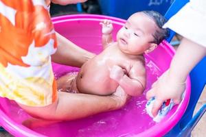 mamá asiática ducha al bebé para limpiar la suciedad dar al niño en un recipiente de baño para la limpieza estilo de vida familiar entre la madre y el niño utilizado para la ducha del bebé productos de crema champús lociones y productos para el cuidado del bebé foto