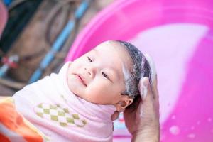 mamá asiática ducha al bebé para limpiar la suciedad dar al niño en un recipiente de baño para la limpieza estilo de vida familiar entre la madre y el niño utilizado para la ducha del bebé productos de crema champús lociones y productos para el cuidado del bebé foto