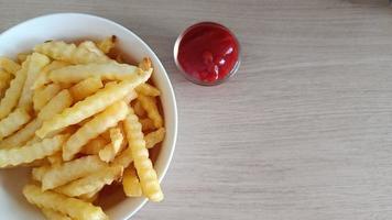 White bowl with fresh cooked french fries potato chips with tomato sauce on wooden background photo