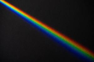 Rainbow streak on black textured paper background photo