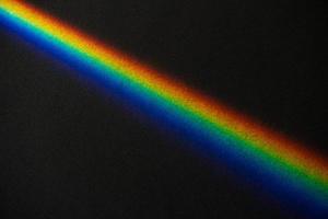 Rainbow streak on black textured paper background photo