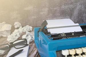 An old blue typewriter and trash paper on wooden desk. Copy space photo