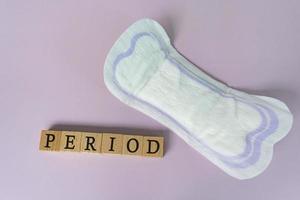 Period text on wooden block. Sanitary pads on purple background. Top view. photo