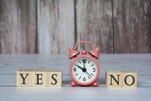 Yes No text on wooden block cube with alarm clock set at 10 o'clock. photo