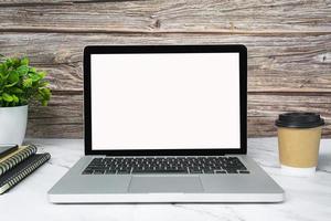 Laptop or notebook with blank screen, coffee, potted plant and notebooks. photo