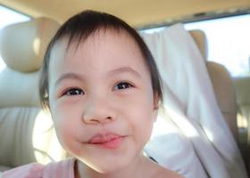 retrato de una graciosa niñita asiática de 3 años sonriendo alegremente en el auto. foto