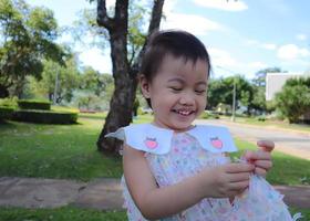 tímida niña caucásica asiática de pie al aire libre mirando su dedo con una gran sonrisa. foto