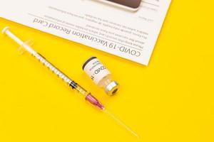 Bottle of Covid-19 coronavirus vaccine and syringe put on yellow background and vaccinated record card with copy space. Concept for spreading of a cure for virus outbreak photo