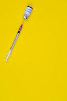 la aguja de la jeringa se inserta en el frasco de la vacuna contra el coronavirus covid-19 sobre fondo amarillo con espacio de copia. tiro de vista superior foto