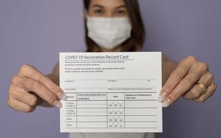 enfoque selectivo en el papel, mujer vacunada con máscara médica que muestra la tarjeta de registro de vacunación del coronavirus covid-19 a la cámara. el concepto de vida después de un brote de virus foto