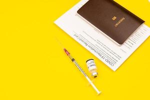 certificado de tarjeta de registro de vacunas covid-19 y pasaporte con frasco de vacuna contra el coronavirus y jeringa juntos sobre fondo amarillo con espacio de copia foto