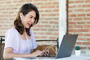 The beautiful middle-aged woman sitting in food shop and working with laptop notebook computer and feel excited with good news on screen. Freelancer job and work from anywhere concept photo