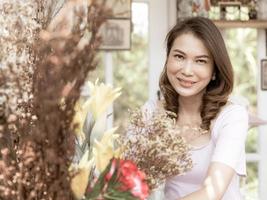 linda y hermosa mujer asiática de mediana edad dueña de una tienda de flores arreglando un montón de flores listas para vender a los clientes. foto procesada en estilo cinematográfico.