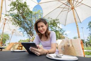 The beautiful middle-aged woman sitting in food shop and working with tablet computer while waiting for food with beautiful blue sky in the background photo