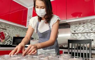 Beautiful Asian housewife wearing protective mask prepares set of banana in coconut milk, famous native Thai style dessert, for sale and delivery to customers for income during coronavirus quarantine photo