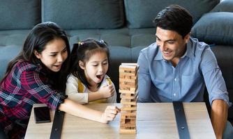 familia de raza mixta, hija y padre caucásico y madre asiática, jugando al juego de madera juntos con fondos y emocionados. foto