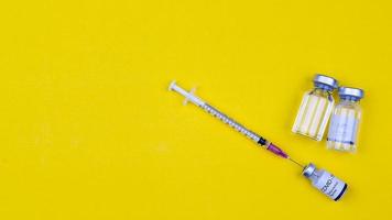 The needle of syringe stab inserts to a bottle of Covid-19 coronavirus vaccine on yellow background with copy space. Top view shot. photo