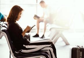 Woman sitting in airport lobby using smartphone and looking at screen while waiting for transit. Sunlight shining from outside photo
