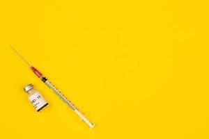 Bottle of Covid-19 coronavirus vaccine and syringe put on yellow background with copy space. Concept for spreading of a cure for virus outbreak photo