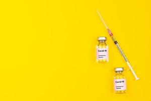 frascos y jeringas de vacuna contra el coronavirus covid-19 juntos sobre fondo amarillo con espacio para copiar. vista superior y toma plana foto
