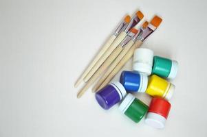 Jars of gouache paint in different colors and synthetic brushes. A set of objects for drawing. Hobbies, creativity, education. Free space for text. photo