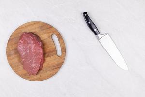 vista superior rebanada de carne de res cruda en la tabla de madera con cuchillo