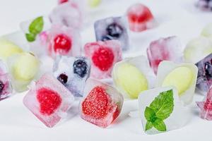 cubitos de hielo con diferentes frutas, menta y bayas congeladas en el interior