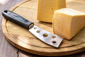 dos trozos de queso y un cuchillo de queso en una tabla de cocina de madera