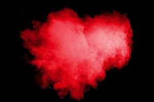 Red heart color powder explosion on black background.Freeze motion of red dust particle splashing. photo