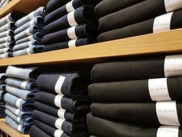 filas de pantalones de mezclilla en los estantes de la tienda de cena o de la tienda minorista. pila de pantalones vaqueros. foto