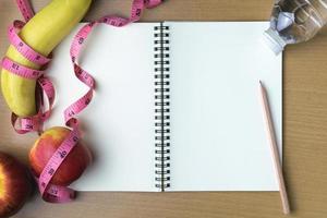 Healthy eating concept, tape measure, fruit and water bottle on a wooden background, blank copy space notebook photo