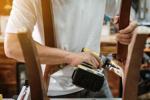 silla de reparación de carpintero y uso de destornillador eléctrico en el taller, concepto de carpintería de restauración de muebles. enfoque selectivo foto