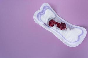 sangre menstrual en una toalla sanitaria sobre fondo morado. directamente arriba. endecha plana foto
