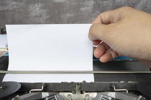 mano tirando de un trozo de papel blanco de una vieja máquina de escribir clásica. copie el espacio foto