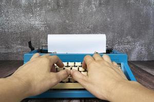 Man at old classic blue typewriter on wooden desk. Business concept. photo